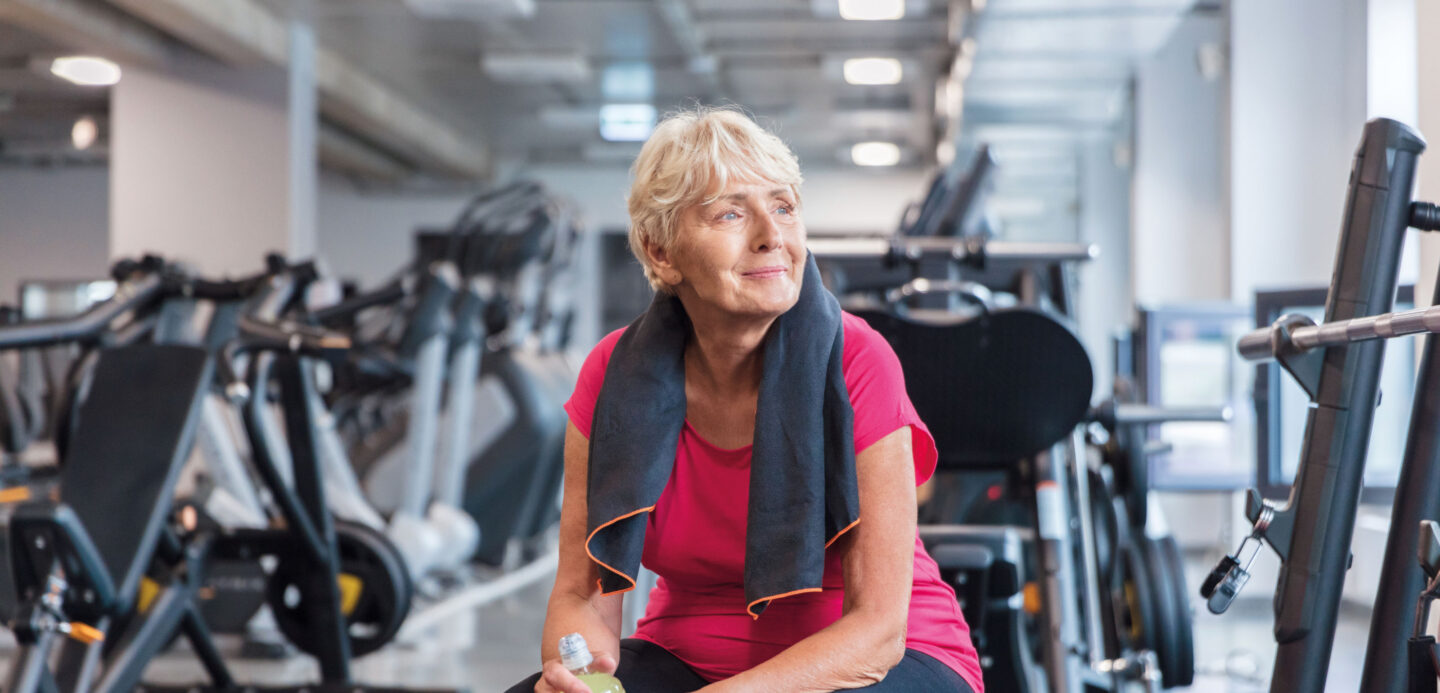 Zufriedene Frau sitzt nach dem Training entspannt im Fitnessraum.
